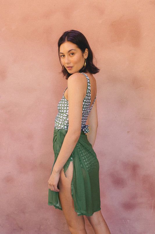 Woman posing wearing a green mesh sarong tied around her waist, with a matching bikini top.