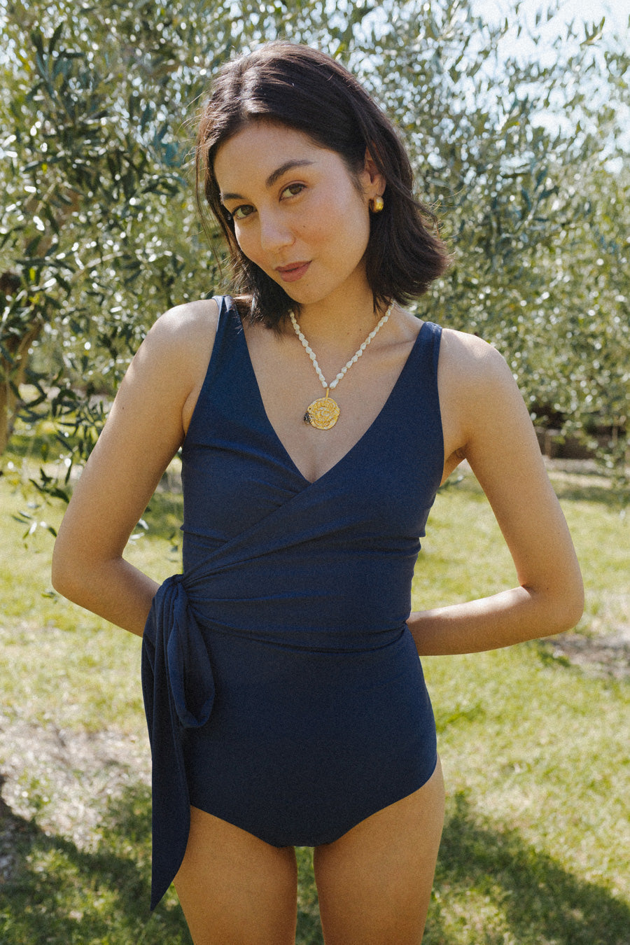 Woman wears a solid navy blue swimsuit with a bow tied at the waist.