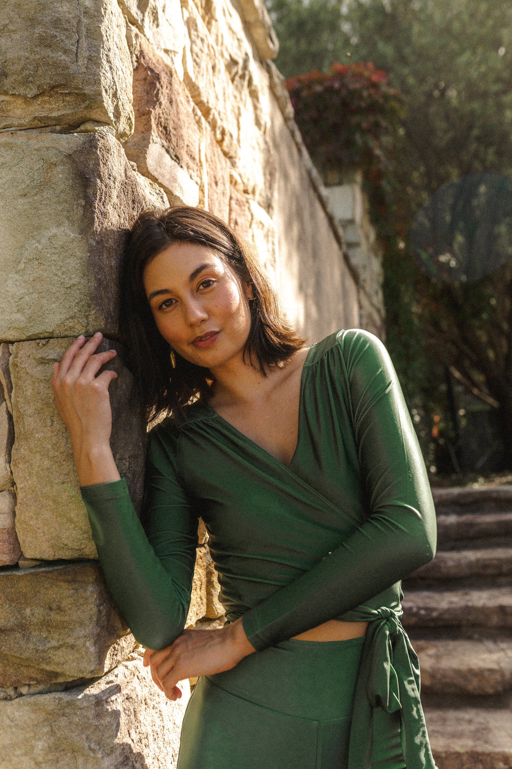 Woman wearing a long sleeve wrap top in a juniper green colour with a v neckline and matching high waisted swim shorts.