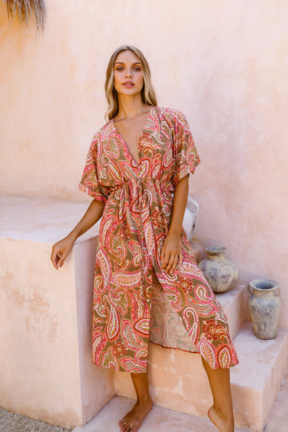 Woman posing in front of stone staircase and artisanal vases dressed in the paisley pink print kaftan dress