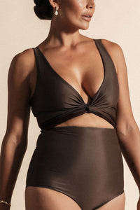 Woman stands in front of a beige background wearing a deep chocolate brown coloured bikini set. The top is cinched at the bust with a tie and the bottoms are high cut.