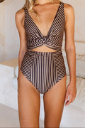 A woman wearing a bikini set with coffee tones and bold black stripes stands in a luxe white resort villa.