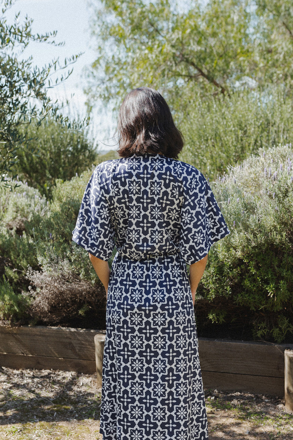 Woman showing the back of a mid-length sleeved navy dress with white detailing.