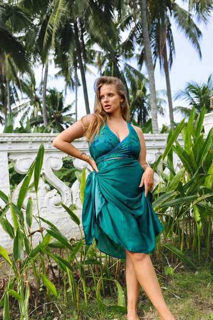 Woman in a tropical garden wearing a printed bikini set with a matching jasmine green sarong tied at the waist.